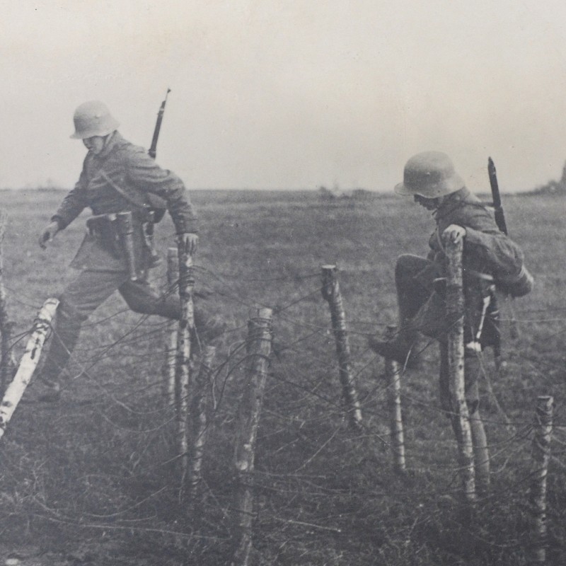 Large-format press photo of German soldiers climbing over barbed wire